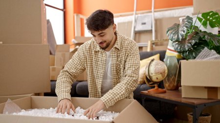 Photo for Young arab man smiling confident unpacking cardboard box at new home - Royalty Free Image