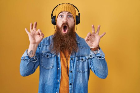 Photo for Caucasian man with long beard listening to music using headphones looking surprised and shocked doing ok approval symbol with fingers. crazy expression - Royalty Free Image
