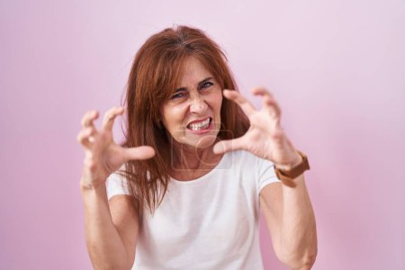 Photo for Middle age woman standing over pink background shouting frustrated with rage, hands trying to strangle, yelling mad - Royalty Free Image