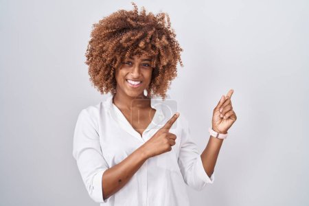 Photo for Young hispanic woman with curly hair standing over white background smiling and looking at the camera pointing with two hands and fingers to the side. - Royalty Free Image