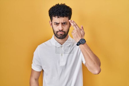 Photo for Arab man standing over yellow background shooting and killing oneself pointing hand and fingers to head like gun, suicide gesture. - Royalty Free Image