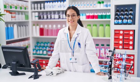 Téléchargez les photos : Jeune belle femme hispanique pharmacien souriant confiance debout à la pharmacie - en image libre de droit