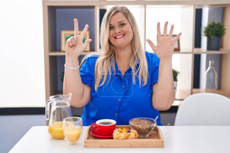 Photo for Caucasian plus size woman eating breakfast at home showing and pointing up with fingers number eight while smiling confident and happy. - Royalty Free Image
