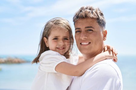 Foto de Padre e hija sonriendo confiados abrazándose en la orilla del mar - Imagen libre de derechos