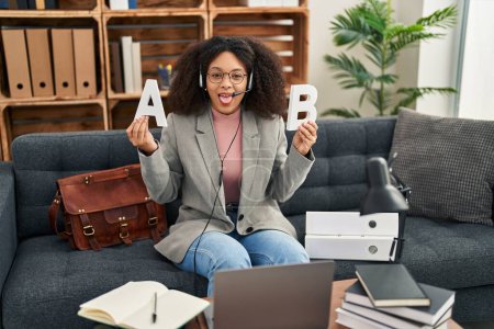 Photo for Young african american woman working speech problems at consultation office sticking tongue out happy with funny expression. - Royalty Free Image