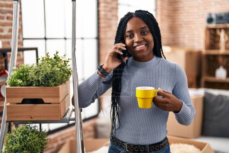 Photo for African american woman talking on smartphone drinking coffee at new home - Royalty Free Image