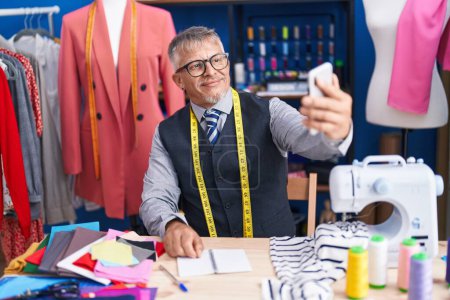 Photo for Middle age grey-haired man tailor smiling confident make selfie by smartphone at clothing factory - Royalty Free Image