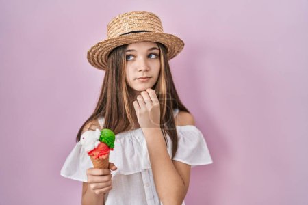 Photo for Teenager girl holding ice cream with hand on chin thinking about question, pensive expression. smiling with thoughtful face. doubt concept. - Royalty Free Image