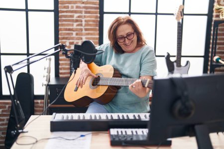 Foto de Senior woman musician smiling confident playing classical guitar at music studio - Imagen libre de derechos