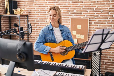 Photo for Young blonde woman musician singing song playing spanish guitar at music studio - Royalty Free Image