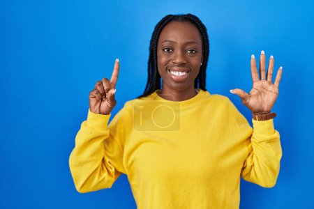 Téléchargez les photos : Belle femme noire debout sur fond bleu montrant et pointant vers le haut avec les doigts numéro six tout en souriant confiant et heureux. - en image libre de droit