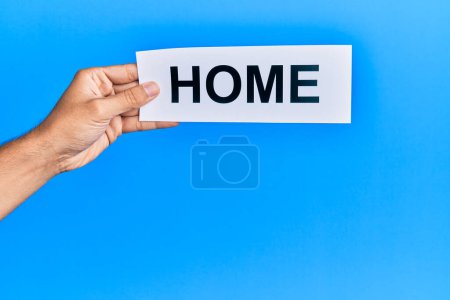 Photo for Hand of caucasian man holding paper with home word over isolated blue background - Royalty Free Image