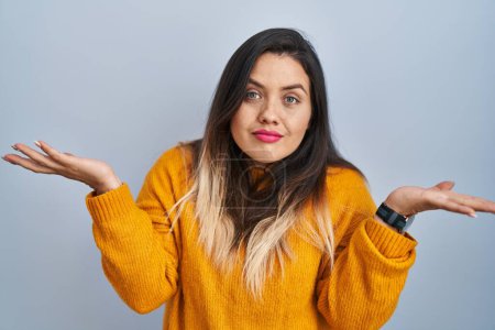 Photo for Young hispanic woman standing over isolated background clueless and confused expression with arms and hands raised. doubt concept. - Royalty Free Image