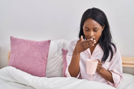 Photo for Young african american woman drinking coffee waking up at bedroom - Royalty Free Image