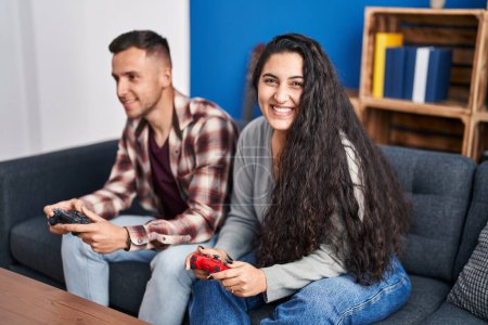 Photo for Man and woman couple playing video game sitting on sofa at home - Royalty Free Image