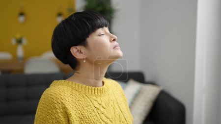 Photo for Young chinese woman sitting on sofa breathing at home - Royalty Free Image