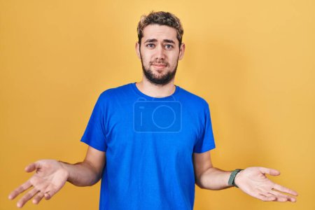 Téléchargez les photos : Homme hispanique avec la barbe debout sur fond jaune inutile et confondu avec les bras ouverts, aucune idée concept. - en image libre de droit