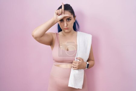Photo for Young modern girl with blue hair wearing sportswear over pink background making fun of people with fingers on forehead doing loser gesture mocking and insulting. - Royalty Free Image
