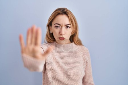 Photo for Hispanic woman standing over blue background doing stop sing with palm of the hand. warning expression with negative and serious gesture on the face. - Royalty Free Image