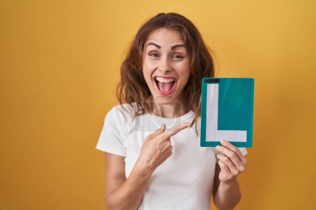 Photo for Beautiful brunette woman holding l sign for new driver smiling happy pointing with hand and finger - Royalty Free Image
