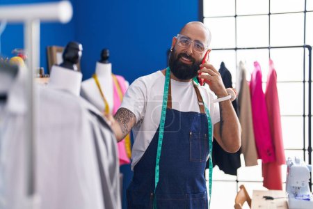 Téléchargez les photos : Jeune homme chauve tailleur parler sur smartphone regarder veste à l'usine de vêtements - en image libre de droit