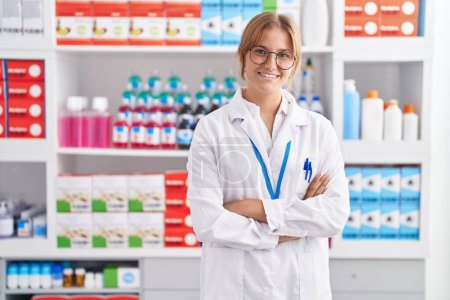 Photo for Young blonde girl pharmacist smiling confident standing with arms crossed gesture at pharmacy - Royalty Free Image