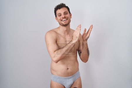 Téléchargez les photos : Jeune homme hispanique debout torse nu portant des sous-vêtements applaudissant et applaudissant heureux et joyeux, souriant mains fiers ensemble - en image libre de droit
