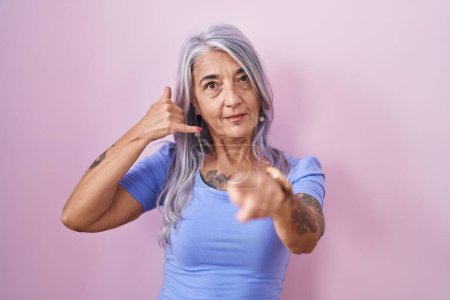 Téléchargez les photos : Femme d'âge moyen avec des tatouages debout sur fond rose souriant faire parler au téléphone geste et vous pointant du doigt. Appelle-moi. - en image libre de droit