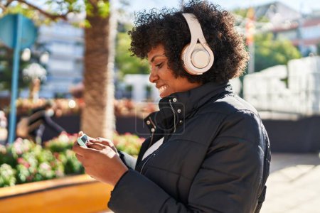 Téléchargez les photos : Afro-américaine femme souriant confiant regarder la vidéo sur smartphone au parc - en image libre de droit