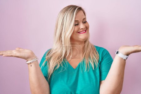 Téléchargez les photos : Femme blanche plus la taille debout sur fond rose souriant montrant les deux mains paumes ouvertes, présentation et comparaison de la publicité et l'équilibre - en image libre de droit