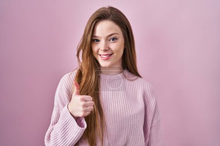 Téléchargez les photos : Young caucasian woman standing over pink background doing happy thumbs up gesture with hand. approving expression looking at the camera showing success. - en image libre de droit