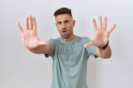 Foto de Hombre hispano con barba de pie sobre fondo blanco haciendo gesto de stop con palmas de las manos, expresión de enojo y frustración - Imagen libre de derechos