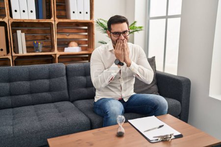 Photo for Young hispanic man with beard working at consultation office laughing and embarrassed giggle covering mouth with hands, gossip and scandal concept - Royalty Free Image
