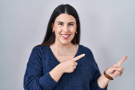Photo for Young brunette woman standing over isolated background smiling and looking at the camera pointing with two hands and fingers to the side. - Royalty Free Image
