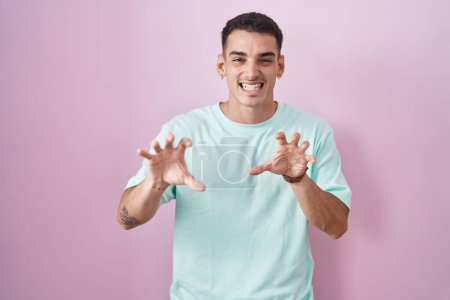 Téléchargez les photos : Bel homme hispanique debout sur fond rose souriant drôle faisant griffe geste comme chat, expression agressive et sexy - en image libre de droit