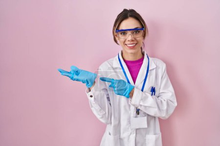 Photo for Hispanic woman wearing scientist uniform amazed and smiling to the camera while presenting with hand and pointing with finger. - Royalty Free Image