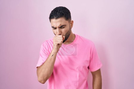 Téléchargez les photos : Jeune homme hispanique debout sur fond rose se sentant mal à l'aise et toussant comme symptôme de rhume ou de bronchite. concept de soins de santé. - en image libre de droit