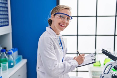 Photo for Young blonde woman scientist writing report working at laboratory - Royalty Free Image