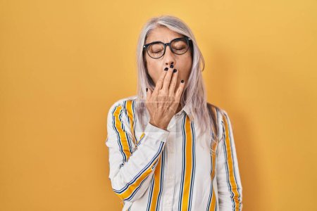 Photo for Middle age woman with grey hair standing over yellow background wearing glasses bored yawning tired covering mouth with hand. restless and sleepiness. - Royalty Free Image