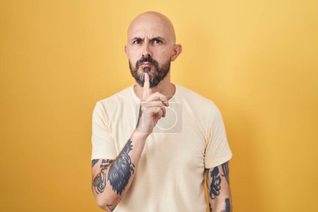 Photo for Hispanic man with tattoos standing over yellow background thinking concentrated about doubt with finger on chin and looking up wondering - Royalty Free Image