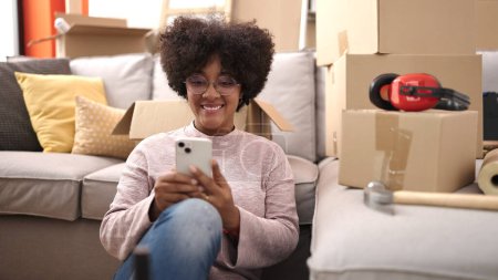 Photo for Young african american woman smiling confident using smartphone at new home - Royalty Free Image
