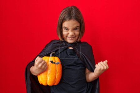 Foto de Pequeño niño hispano usando una capa y sosteniendo la calabaza de halloween cara seria pensando en la pregunta con la mano en la barbilla, pensativo acerca de la idea confusa - Imagen libre de derechos
