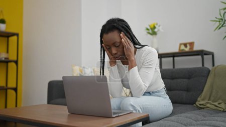 Foto de Mujer afroamericana usando laptop con expresión estresada en casa - Imagen libre de derechos