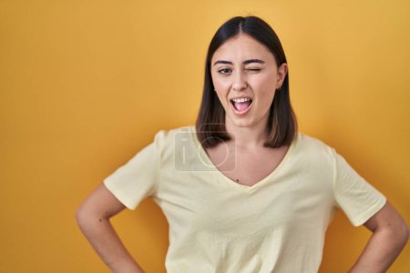 Photo for Hispanic girl wearing casual t shirt over yellow background winking looking at the camera with sexy expression, cheerful and happy face. - Royalty Free Image