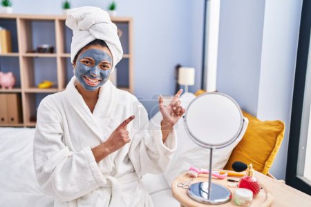 Photo for Hispanic woman with dark hair wearing beauty face mask smiling and looking at the camera pointing with two hands and fingers to the side. - Royalty Free Image
