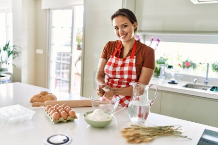 Téléchargez les photos : Young beautiful hispanic woman smiling confident mixing bread dough on bowl at the kitchen - en image libre de droit