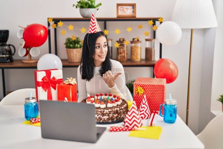 Téléchargez les photos : Femme hispanique célébrant anniversaire avec un gros gâteau au chocolat faire appel vidéo pointant pouce vers le côté souriant heureux avec bouche ouverte - en image libre de droit