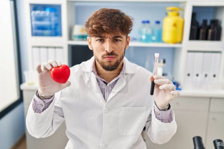 Photo for Arab man with beard working at scientist laboratory holding blood samples skeptic and nervous, frowning upset because of problem. negative person. - Royalty Free Image