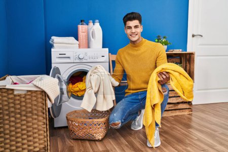 Photo for Young hispanic man smiling confident washing clothes at laundry - Royalty Free Image