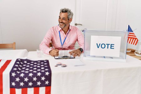 Foto de Hombre de pelo gris de mediana edad presidente de la mesa electoral escribiendo en portapapeles en el colegio electoral - Imagen libre de derechos